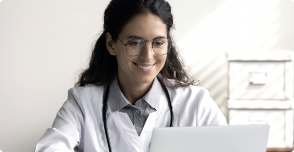 Female medical professional wearing glasses smiling at laptop