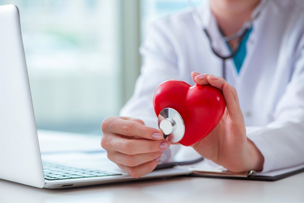 a doctor holding a red heart with a stethoscope in front of a laptop